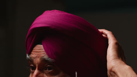 Close-Up-Low-Key-Studio-Lighting-Shot-Of-Senior-Sikh-Man-With-Beard-Using-Salai-Needle-When-Putting-On-Turban-Against-Dark-Background